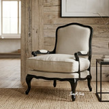 Cannes Occasional Armchair featuring carved black armrests and neutral linen seating in a warm styled living room with art and wood panelling