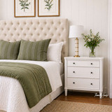 An upholstered tufted linen headboard in cream, showed from an angled view, showcasing its texture and detailing.