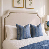 A close-up detailed angled view of a cream linen upholstered headboard in neutral linen tones, with studding detail, in an elegantly styled Hamptons inspired bedroom.