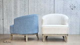 Rear and side view of the two chairs, one in blue chenille and the other in beige cream linen upholstery finish, placed back-to-back. This perspective emphasizes the differences in the upholstery and the weathered oak legs, offering a comprehensive comparison of the finishes.