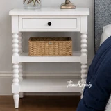 A front view of the Montclair Side Table in White showcasing its bobbin leg detailing and functional drawer and display shelving.
