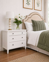 An angled view of a white three drawer Hamptons bedside table, perfect as a bedside or side table with storage.