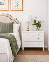 A white bedside table with drawers, perfectly complementing Hamptons-style interiors.