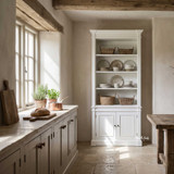 Tall white single bookcase displaying ceramic dinnerware and glassware in a warm rustic kitchen