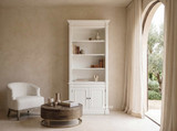 Thomas and Hurley white timber single bookcase wall unit styled with books and ceramic decor in a warm living space with linen armchair