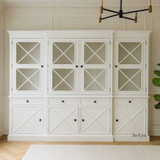 Somerset 4 Door Display Wall Unit in situ in living room, highlighting its Hamptons-inspired design, signature cross detailing on the doors, and spacious shelving, perfect for use as a display unit or bookshelf.