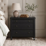 Brynmore black bedside table front view showing three drawers in a styled bedroom
