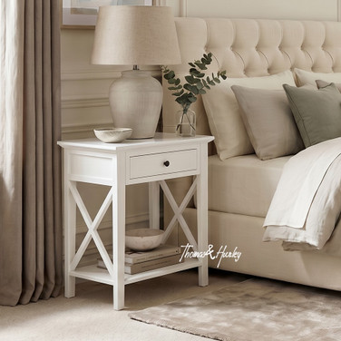 Hampstead 1 Drawer Bedside Side Table in white styled beside a bed with a ceramic lamp, eucalyptus vase and open shelf with stacked books in a modern Hamptons bedroom.
