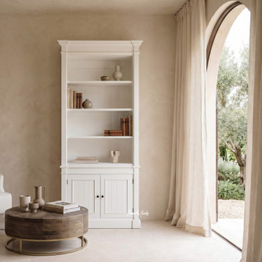 Hamptons-style white bookcase cabinet with storage in a styled living room with coffee table and arched entryway