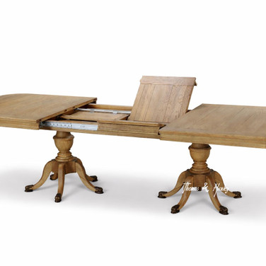 Detailed image of the Berkshire Double Extension Dining Table by Thomas & Hurley in oak, fully extended with twin pedestal base and brass feet, showing leaf detail.