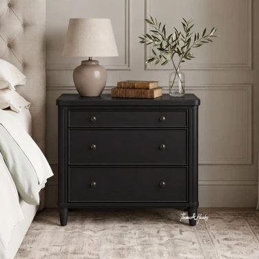 Brynmore black bedside table front view showing three drawers in a styled bedroom