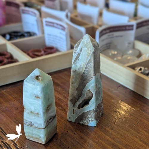 Two Caribbean Blue Calcite towers with ocean-blue and sandy brown bands displayed on a wooden surface at Prana Blessings Metaphysical Shop in Santa Fe — crystal points that promote calm, clarity, and higher consciousness. Two Caribbean Blue Calcite towers with ocean-blue and sandy brown bands displayed on a wooden surface at Prana Blessings Metaphysical Shop in Santa Fe — crystal points that promote calm, clarity, and higher consciousness.