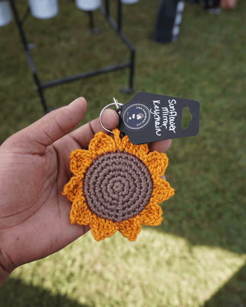 A handmade crochet sunflower keychain with a mirror behind it