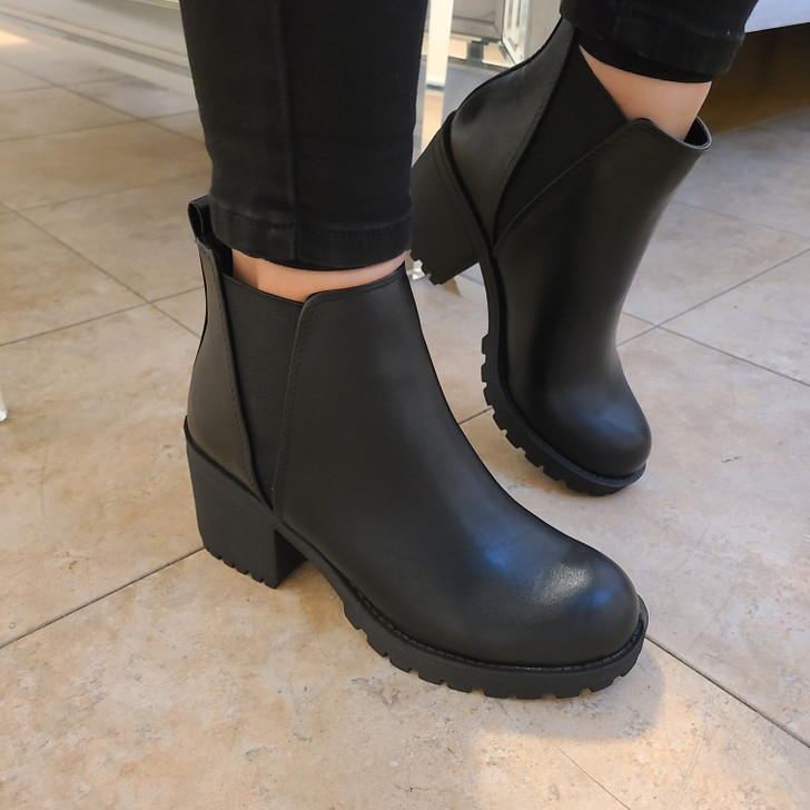 The model is wearing a pair of black ankle boots. The boots have a sleek design, made of smooth, matte faux leather material. They feature chunky heels that add height while ensuring comfort.