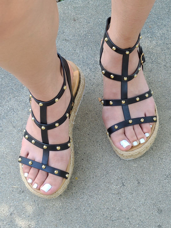 A pair of stylish black strappy sandals adorned with golden studs, featuring a comfortable espadrille sole and perfect for a casual yet elegant summer look.