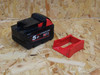 Milwaukee M18 battery and red metal mount on a wooden surface, six pack included.