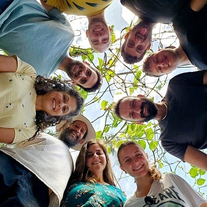 A group of nine people stands in a circle outdoors, smiling and gathered around plant, celebrating an innovative, soil-free plant nurturing approach.