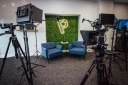 Video production studio with cameras, teleprompters, microphones, lights, and two blue chairs.
