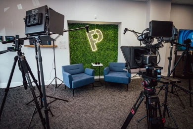 Video production studio with cameras, teleprompters, microphones, lights, and two blue chairs.