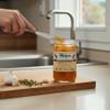 Fisher’s Garlic Jam being spread with a knife on a wooden board with fresh garlic and herbs.