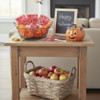 A light wooden living room end table with a bowl of Red Macintosh Apple Orchard Caramel Apple Suckers, a pumpkin candy dish and a "Happy Halloween sign. A large basket of Macintosh Apples is on the bottom shelf of the table.