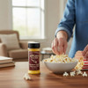 Amish Country Ballpark Style Popcorn Salt 5.5 oz shaker beside bowl of popcorn being seasoned on kitchen table