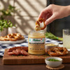 Fisher’s Sweet Mustard-Style Dip with pretzels and sliced sausage on a wooden board at an outdoor table.