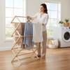 Natural wood folding clothes drying rack with laundry hanging in a sunlit home laundry room