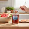 A jar of Harvest Array Watermelon Preserves sits on a light wooden table beside a plate of toast with a spread of the watermelon preserves and a bowl of  watermelon  slices.