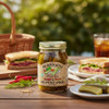 Sweet and spicy dill pickle spears jar on an outdoor picnic table with sandwiches, fresh dill, chili peppers, and iced tea in the background.