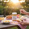 Bone Suckin’ Mustard on a picnic table with hot dogs, chips, coleslaw, and watermelon at sunset.
