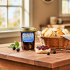 Blue Ridge Jams Boysenberry Preserves Jar on a wooden table next to a basket of buttermilk biscuits. A biscuit is cut in half with boysenberry preserves spread on it with a knife.