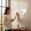 Woman hanging a white WNC Strong North Carolina sign on a shiplap wall while holding a coffee mug
