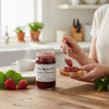 Annie’s Kitchen Strawberry Rhubarb Jam being spread on toast with fresh strawberries and tea on a wooden table.