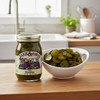 A jar of  Jake & Amos Lime Pickles next to a bowl of the green pickles on a wooden kitchen counter in a bright country style kitchen.