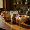 A rustic kitchen with a wooden kitchen table set with a package of Double L Ranch Five Bean Soup Mix, a basket of crusty bread and a bowl of Five Bean Soup for a hearty lunch or dinner.
