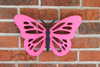 Fuchsia pink hanging butterfly displayed on a brick wall.