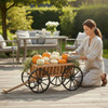 Woman arranging small pumpkins in a wooden garden wagon with black metal wheels on a sunny patio