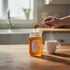 Pure mountain honey jar with honey dipper drizzling into hot tea in a bright kitchen scene