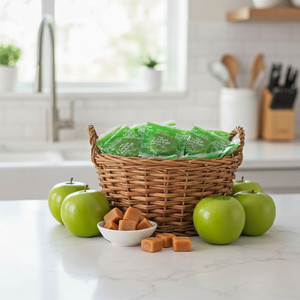 A bright Kitchen with a white granite island. On the island is a basket of Green Apple  Apple Orchard Caramel Apple Suckers, a few green apples, and a dish of caramel squares.