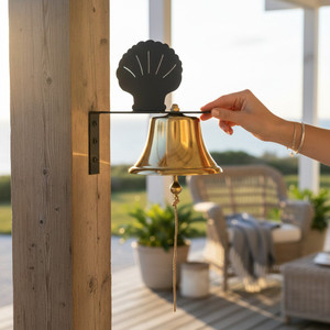 Brass patio bell with scallop shell silhouette bracket on porch post overlooking coastal deck and ocean scene
