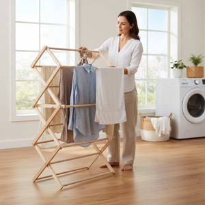 Natural wood folding clothes drying rack with laundry hanging in a sunlit home laundry room