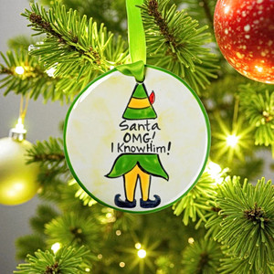 Hand-painted Christmas ornament with elf design and text 'Santa OMG! I Know Him!' hanging on a tree. Order today from Harvest Array.