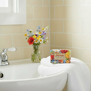 American Wildflower 2 oz. mini Shea Butter Soap on a white towel placed on a white powder room sink with a vase of matching wildflowers nearby.