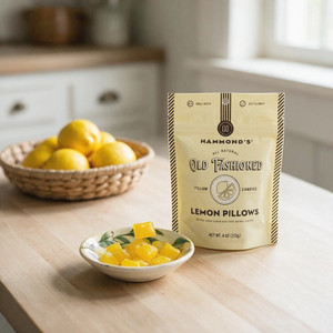A sunny kitchen with a wooden kitchen island. On the counter are a bag of  Hammond's Lemon Pillow Drops Candy, a lemon design candy dish with lemon pillow candies in it, and a basket of lemons.