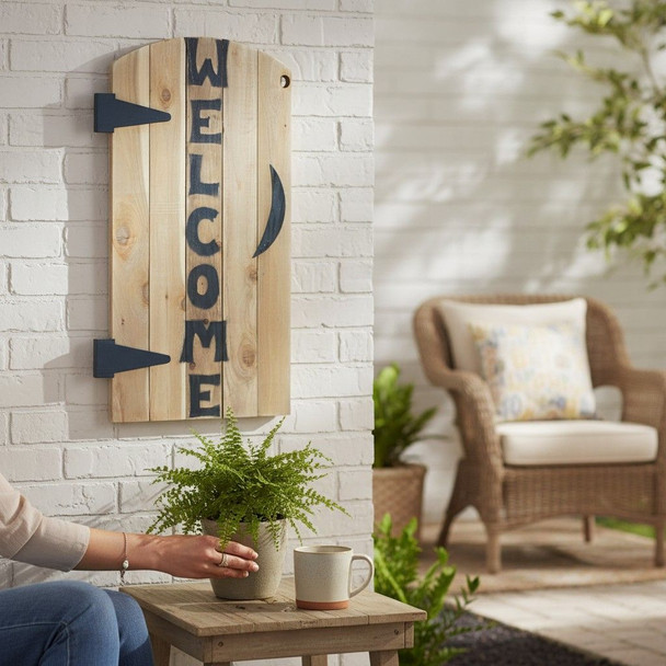 Wooden vertical welcome sign with blue accents hanging on a white brick wall in a cozy outdoor seating area