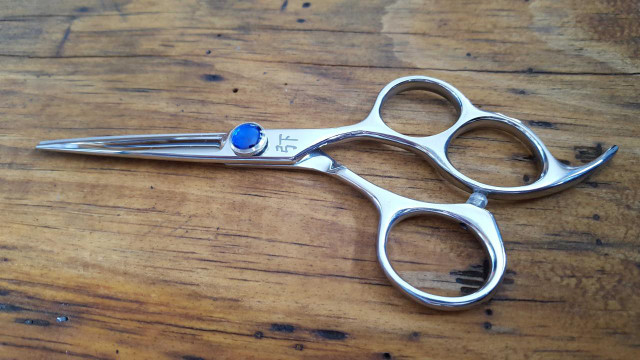 Shear Fanatic™️ Scissor Shear Fanatic®️ Pro Series 3 Hole Hair Cutting Shears, professional hair scissors with a sleek metallic design and finger holes, placed on a wooden surface.