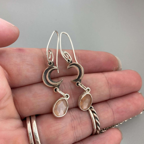 Hand cut sterling silver crescent moon drops showcasing genuine bezel set peach moonstones.  The earrings hang from sterling silver handmade earwires.