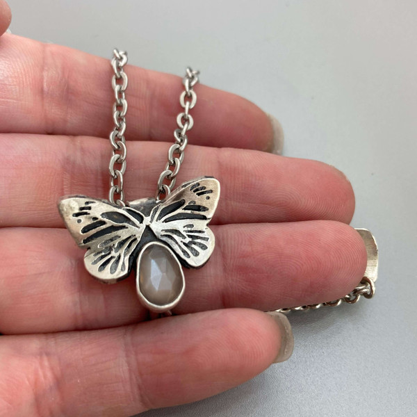 Hand cut sterling silver monarch butterfly pendant showcasing a genuine bezel set peach moonstone.  The pendant hangs from a stainless steel chain finished with a sterling silver lobster clasp.