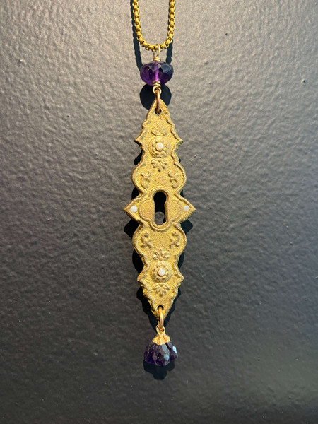 Antique cast brass escutcheon set with fire opals and embellished with amethysts hanging on 26” long brass box chain.